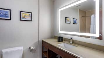 A bathroom with a toilet, sink, and mirror. There are framed pictures on the wall.