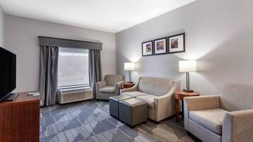 Une chambre d’hôtel équipée d’un téléviseur à écran plat, d’un canapé, de deux fauteuils, d’une table basse, d’un bureau et d’une fenêtre avec des rideaux.