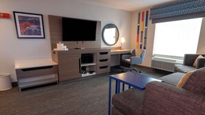 A hotel room with a flat-screen TV, a desk with a computer, a chair, a sofa, and a small table.