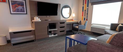 A hotel room with a flat-screen TV, a desk with a computer, a chair, a sofa, and a small table.