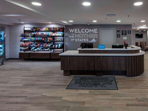 A hotel reception area with a 'Welcome to the Mother of States' sign, a self-service kiosk, and a snack display.