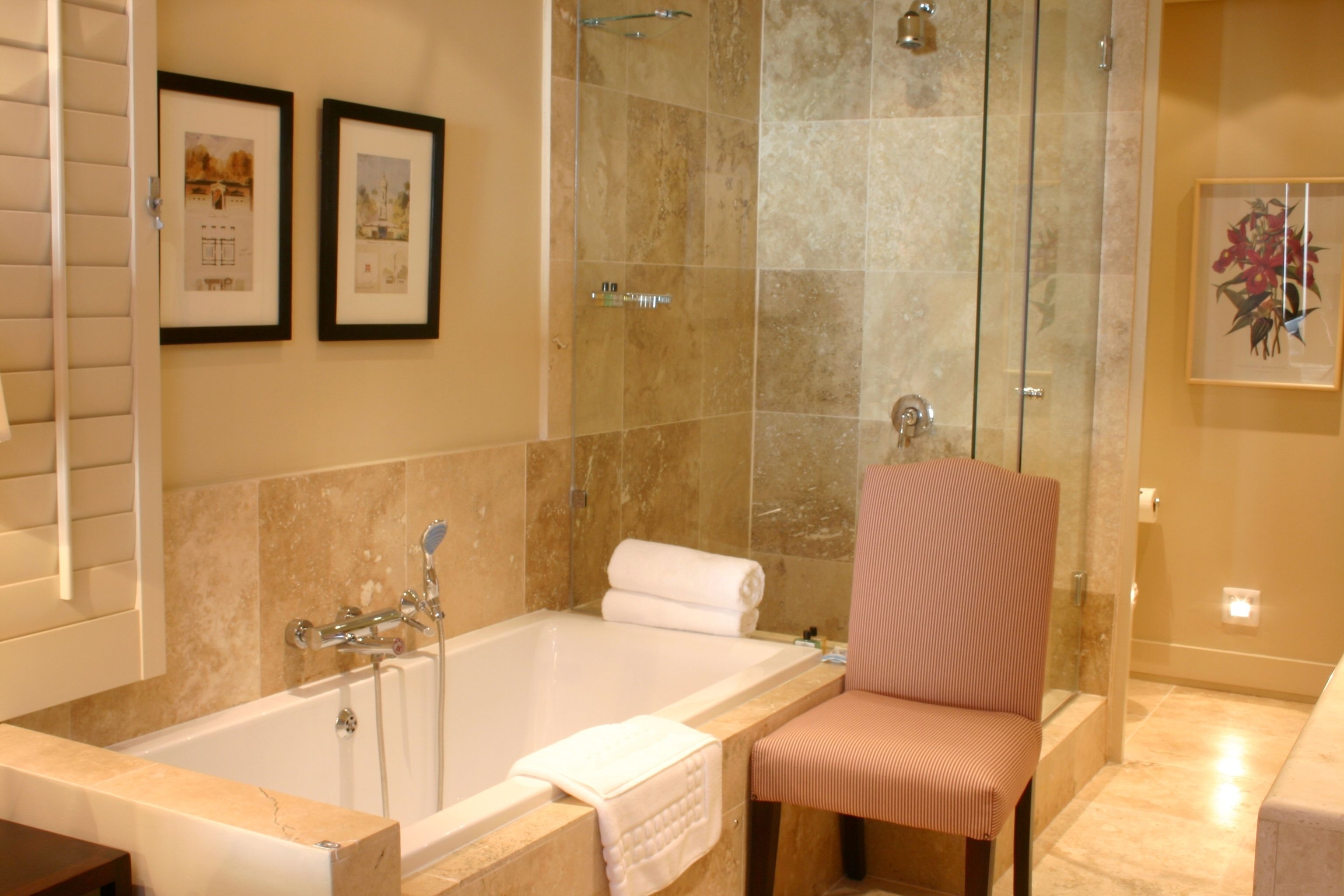 Une salle de bain avec une baignoire, une douche, une chaise et des tableaux encadrés au mur.