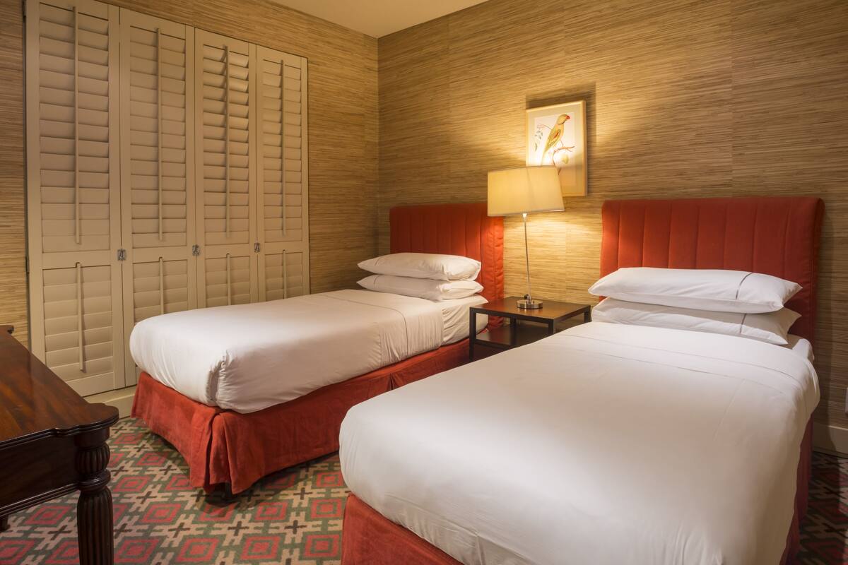 A hotel room with two beds, a wooden wardrobe, a lamp, and a patterned floor.