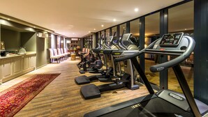 Une salle de sport équipée de tapis de course, de vélos elliptiques et d’autres appareils de musculation. On y trouve un comptoir d’accueil et un espace détente avec des chaises.