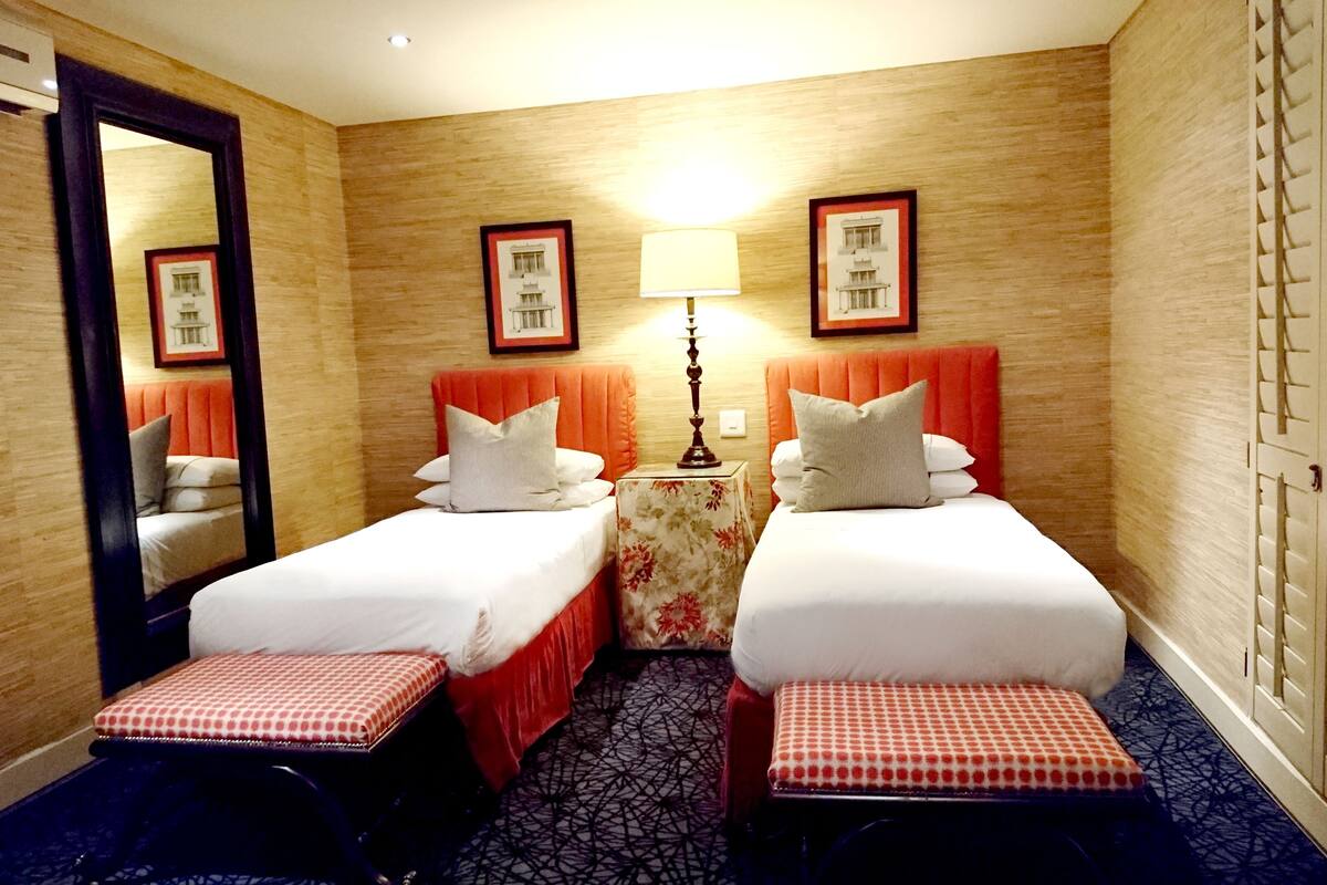 A hotel room with two single beds, a small table with a lamp, and a mirror.