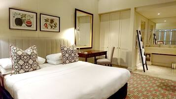 A hotel room with a large bed, a desk, a chair, a mirror, and two framed botanical prints on the wall.