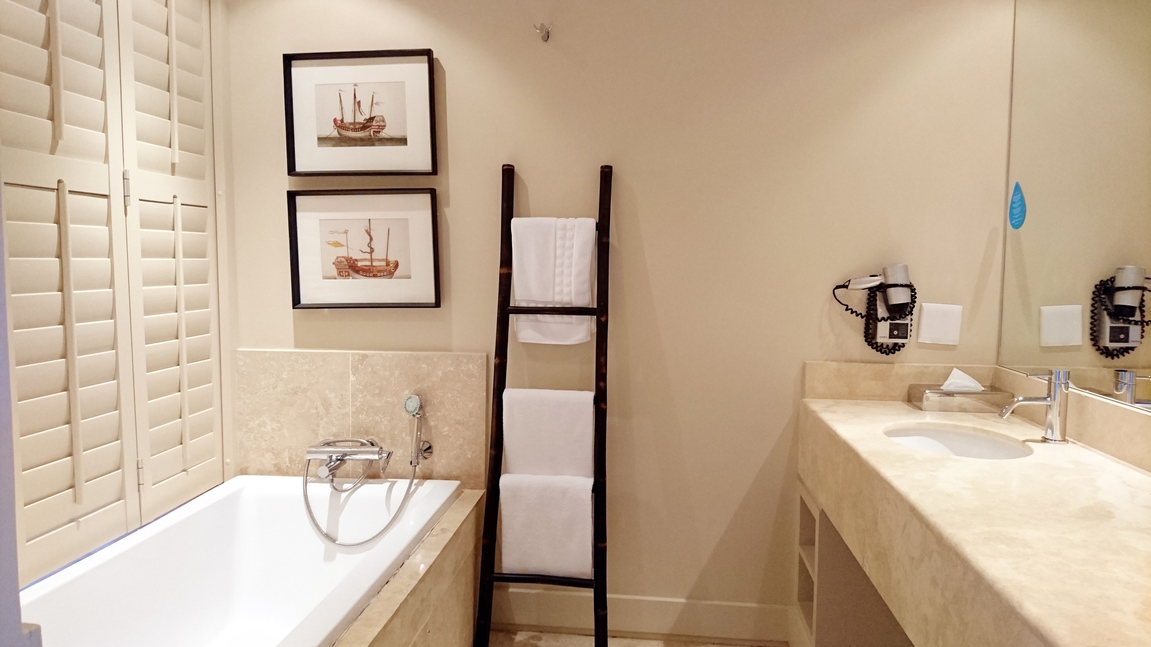 Een moderne badkamer met een bad, een douche en een wastafelmeubel. Er hangen afbeeldingen in lijsten aan de muur en een handdoekrek.