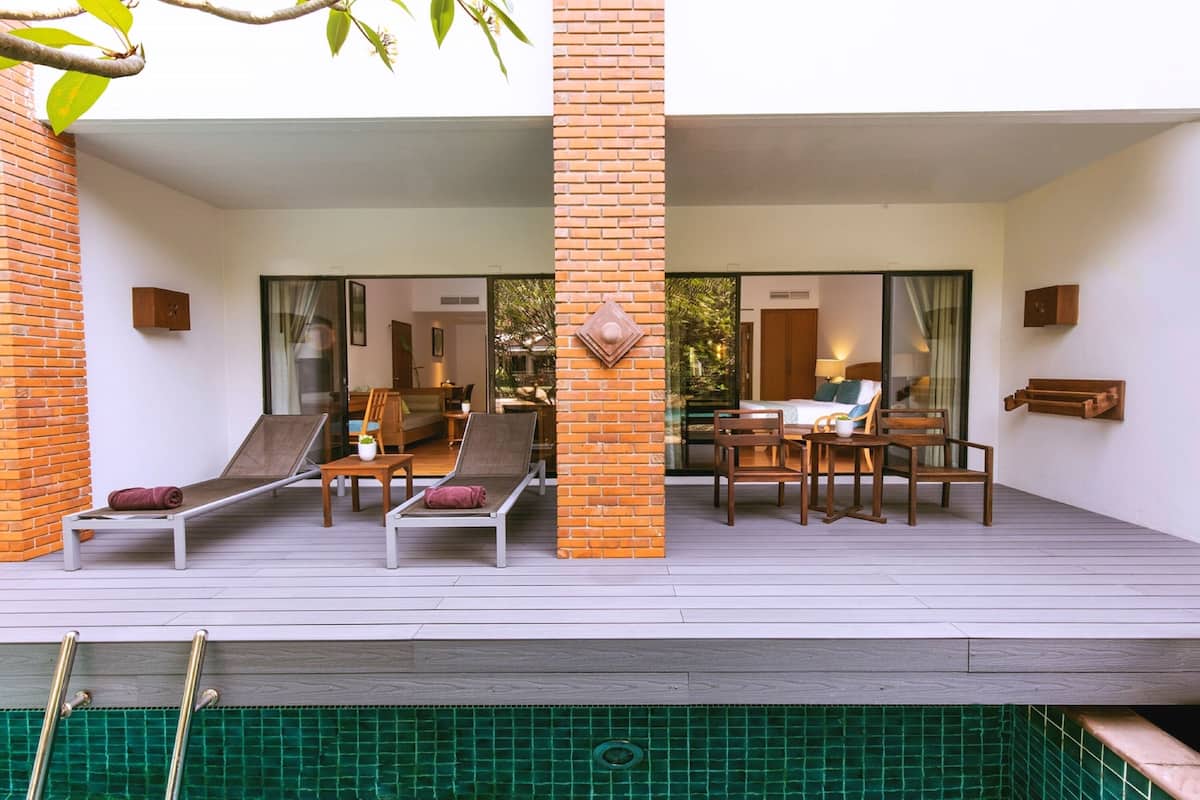 Un espace de détente extérieur moderne, doté de deux chaises longues, d’une table en bois et de chaises, avec vue sur une piscine.
