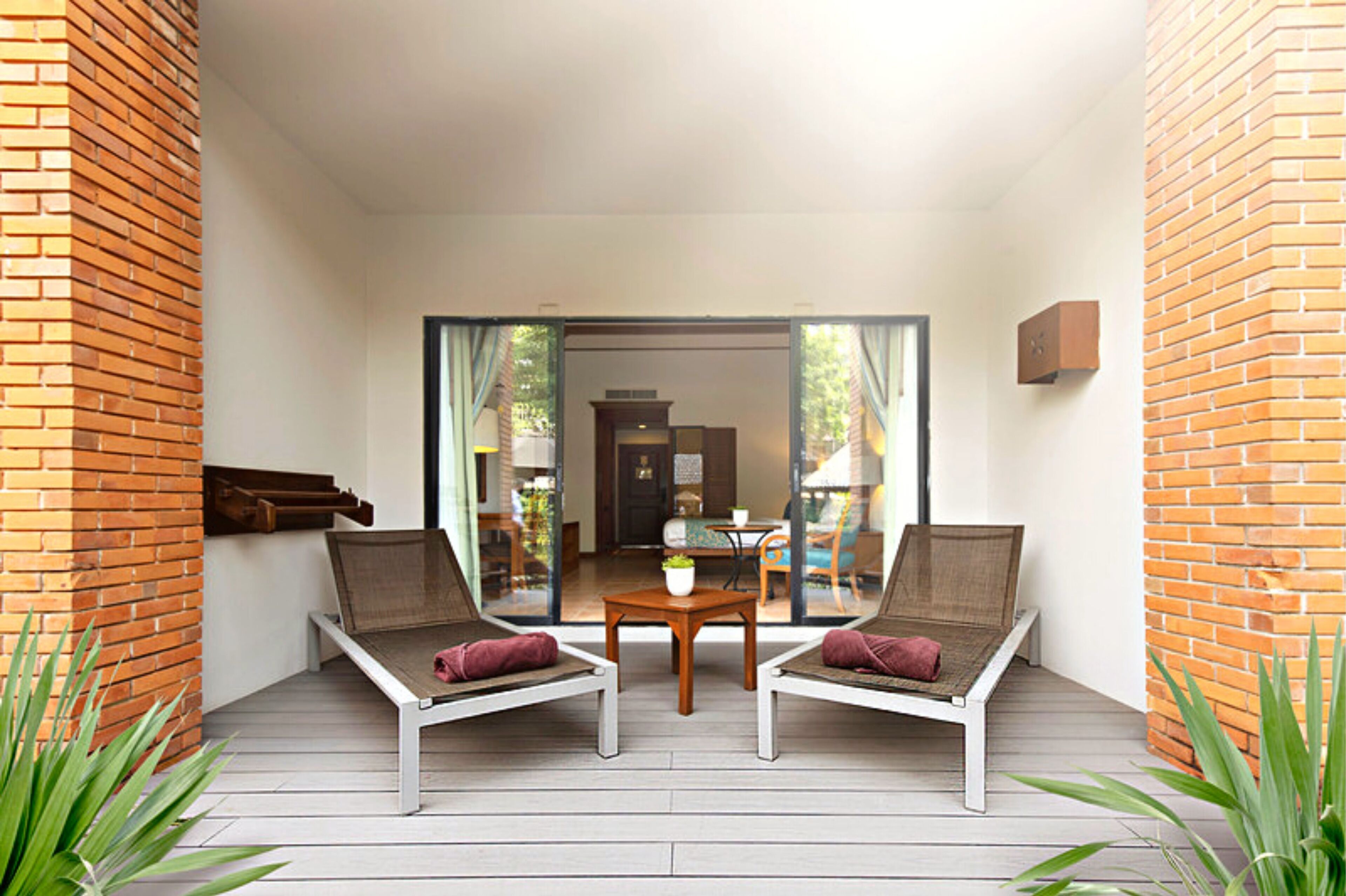 A balcony with two lounge chairs, a small table, and a view of an indoor dining area.