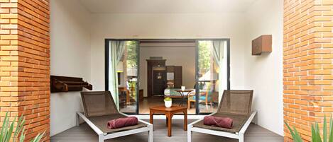A balcony with two lounge chairs, a small table, and a view of an indoor dining area.