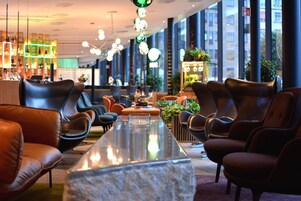 Un área de descanso moderna con sillones de cuero, una mesa central y amplios ventanales con vistas a la ciudad.