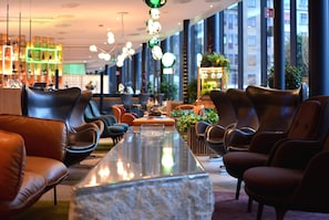 Un área de descanso moderna con sillones de cuero, una mesa central y amplios ventanales con vistas a la ciudad.