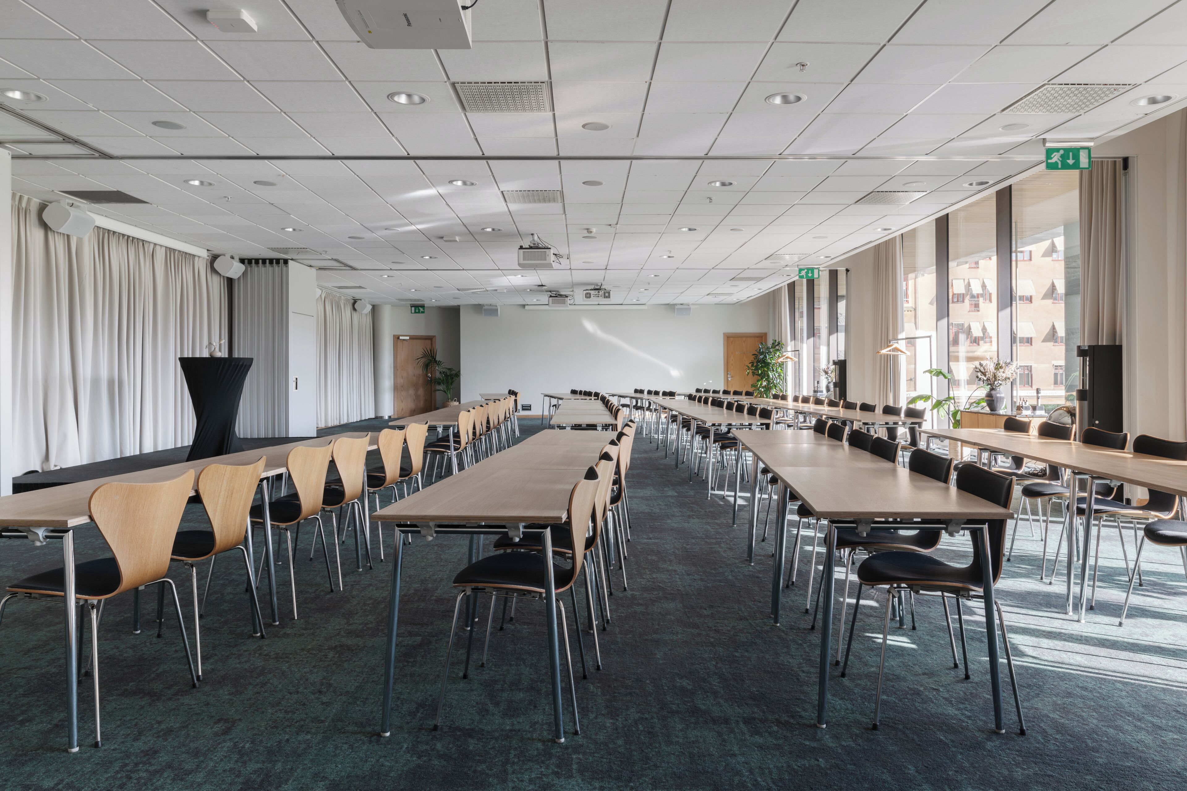 A conference room with long tables and chairs, large windows, and a carpeted floor.