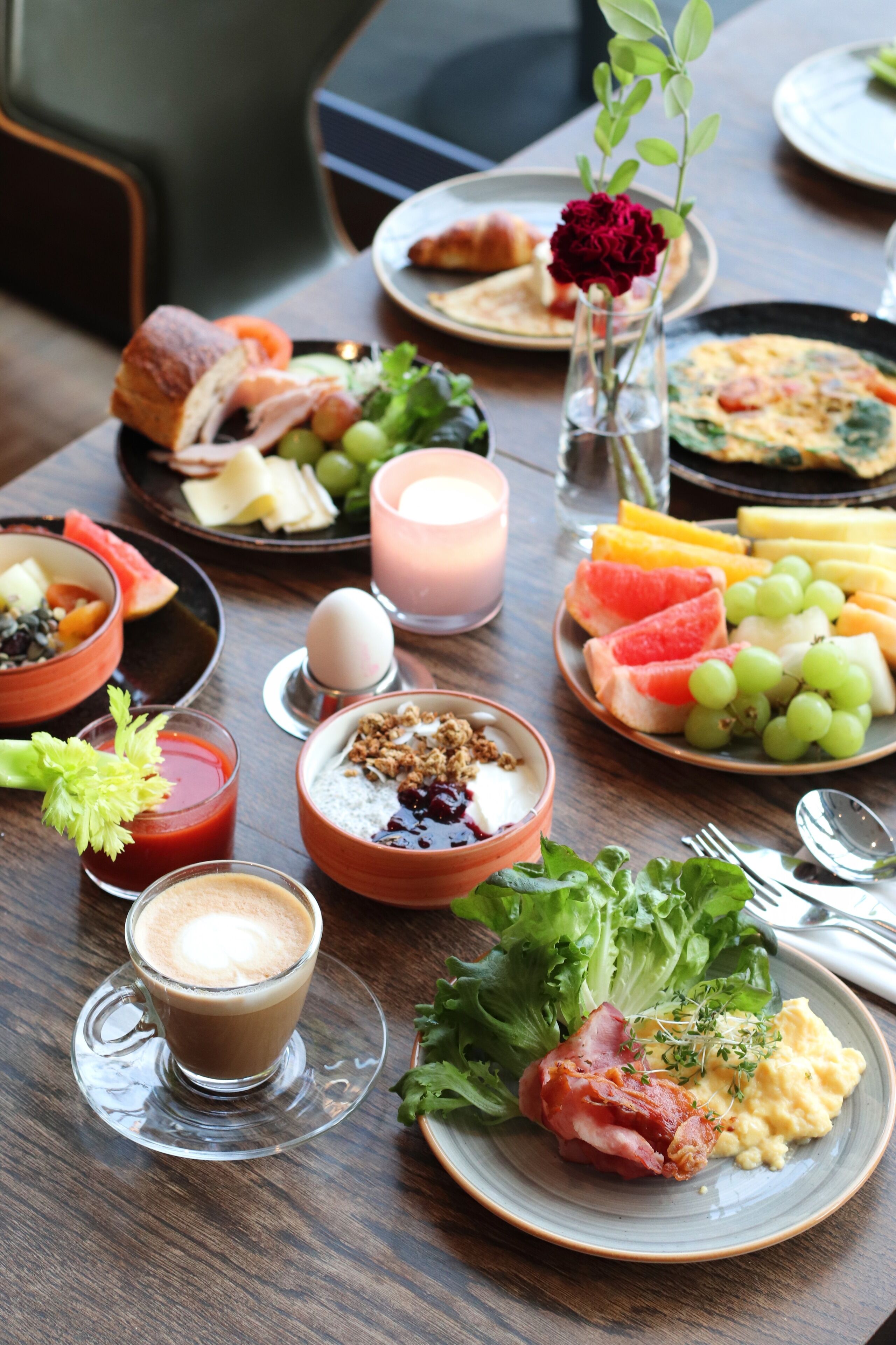 A breakfast setting with various dishes, including eggs, toast, and fruit, on a wooden table.