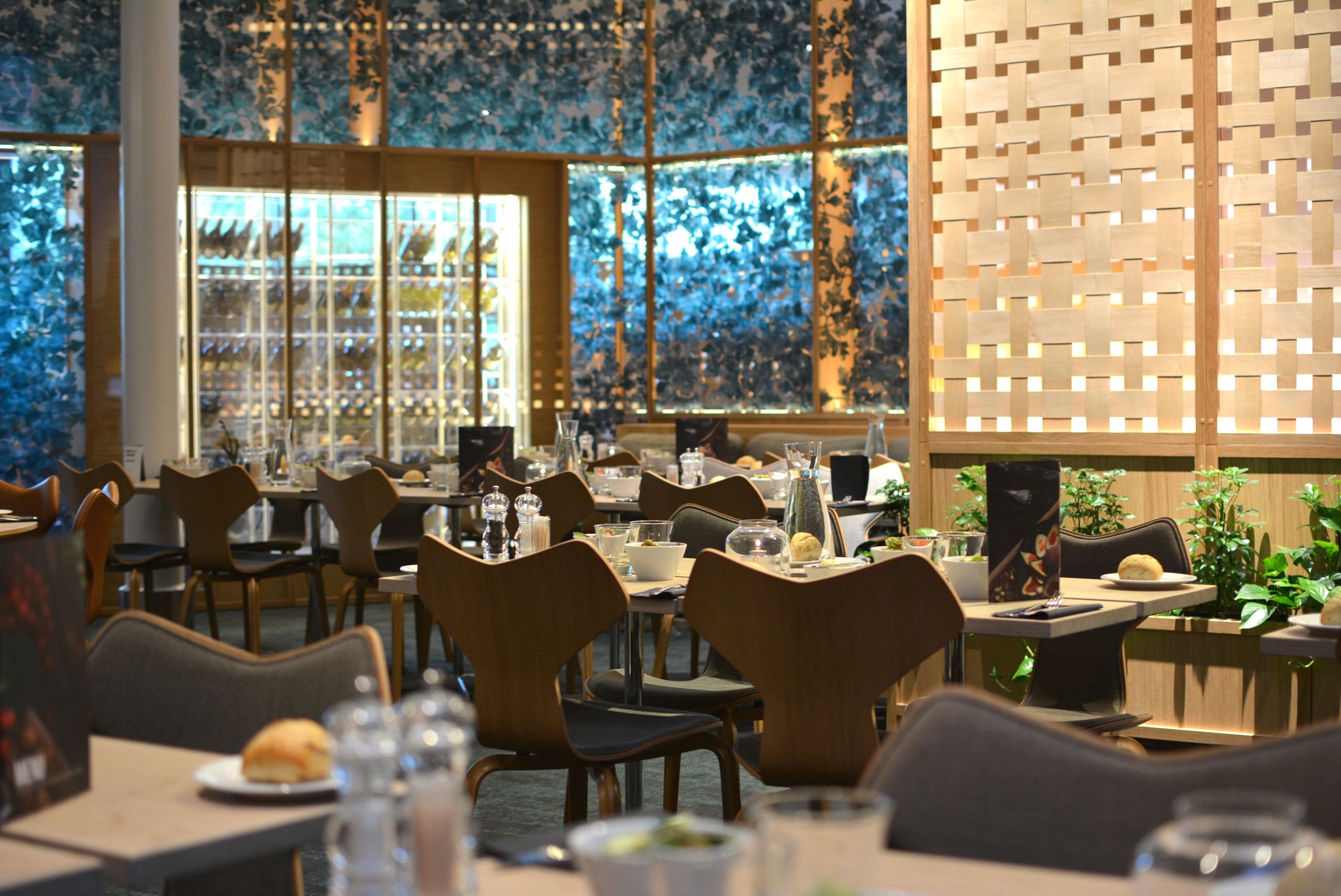En restaurang med flera bord och stolar, ett stort fönster med utsikt och en dekorativ vägg.