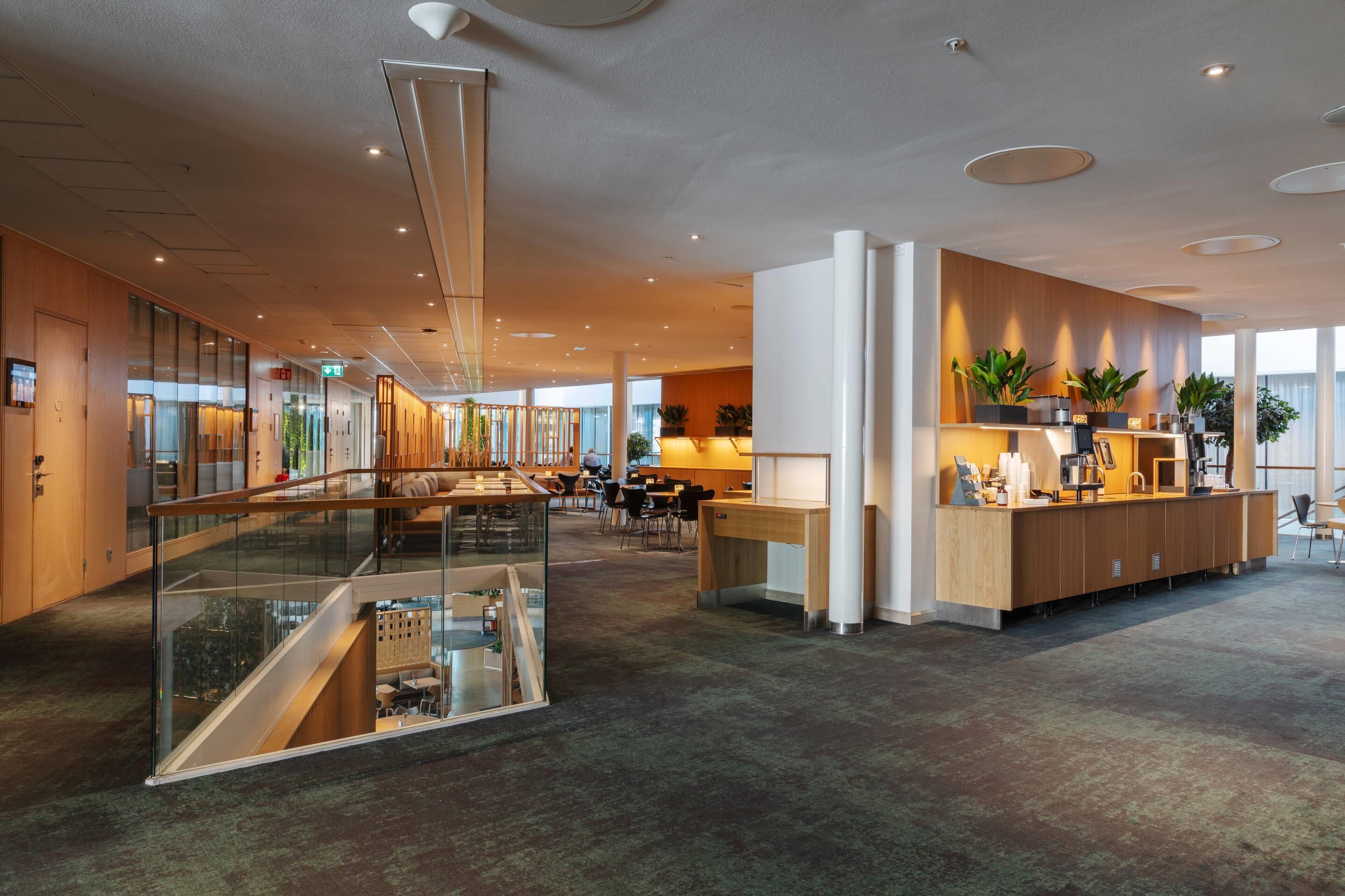 Eine moderne Hotelhalle mit Glasatrium, Holzbuffet und einer Sitzecke.