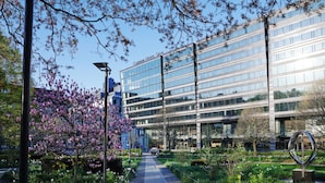 A modern hotel with a glass facade, a central pathway, and a well-maintained garden with flowering trees. - Clarion Hotel Sign (Stockholm)