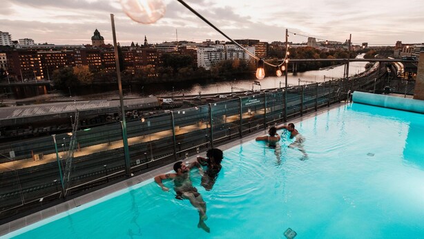 A swimming pool with a cityscape view, including a bridge and buildings in the background. - Clarion Hotel Sign (Stockholm)