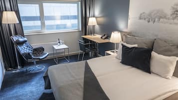 Une chambre d’hôtel avec un lit, un bureau, une chaise et une fenêtre.