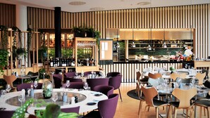 A restaurant with round tables, purple chairs, and a bar area. - Clarion Hotel Sign (Stockholm)
