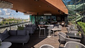 A rooftop terrace with outdoor seating, a view of the city, and a modern building structure. - Clarion Hotel Sign (Stockholm)