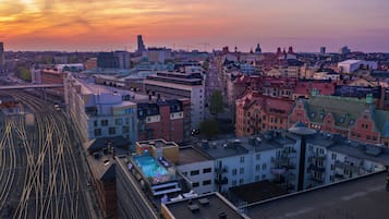 Un paisaje urbano al atardecer con una vía de tren destacada y un edificio con piscina en la azotea.
