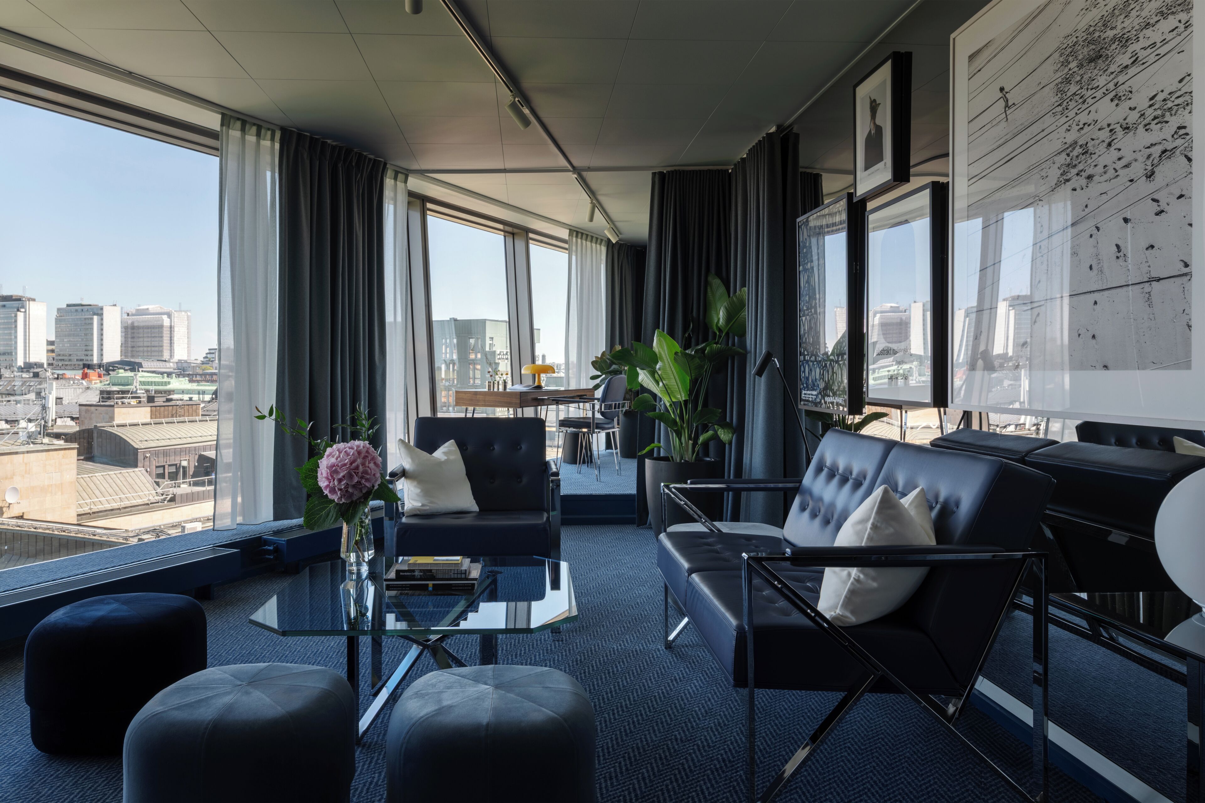 A modern hotel room with a city view, a sofa, a coffee table, and a dining area.