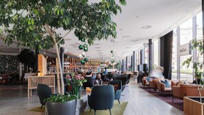 A modern indoor space with seating areas, a bar, and large windows. - Clarion Hotel Sign (Stockholm)