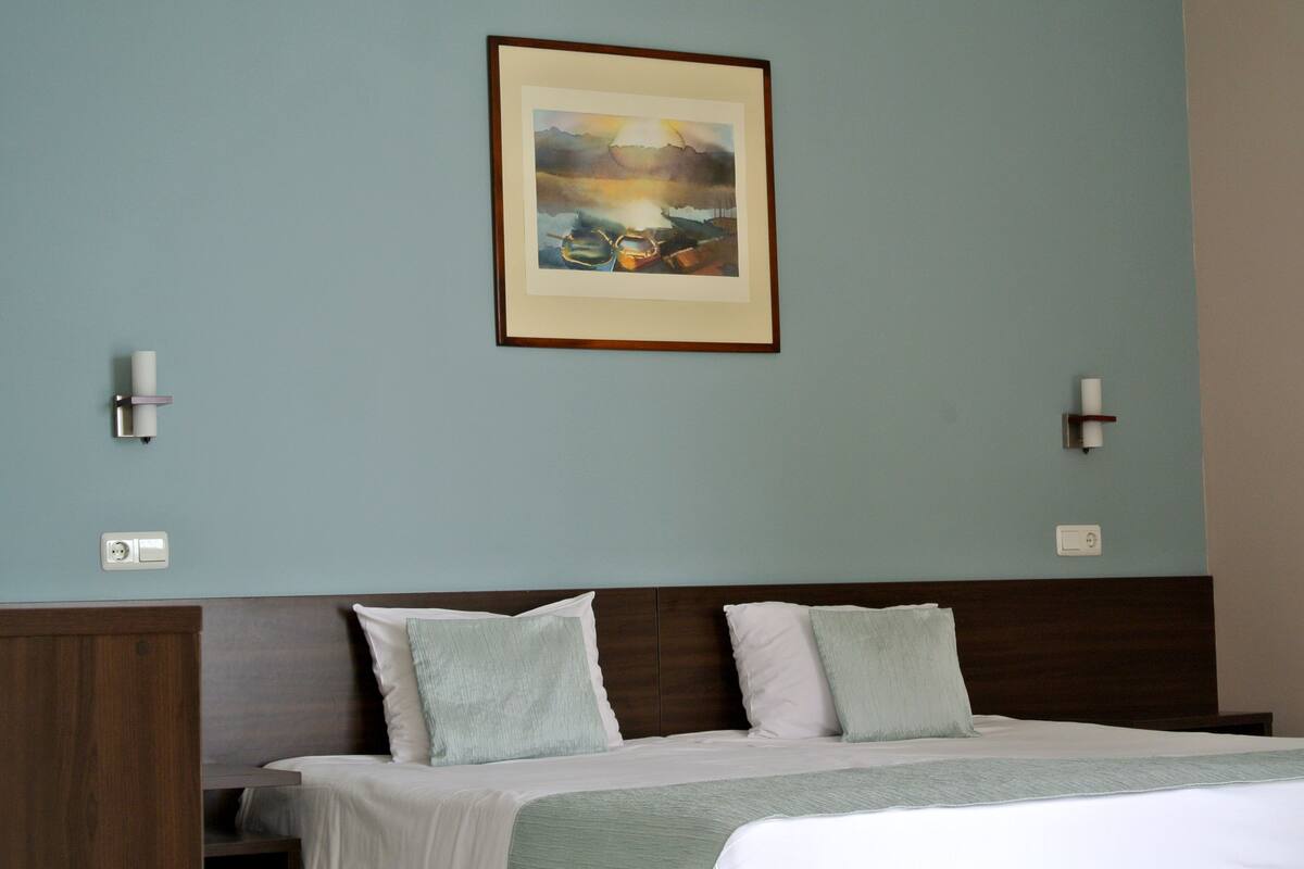 A hotel room with a bed, two wall sconces, a painting, and a night switch on the wall.