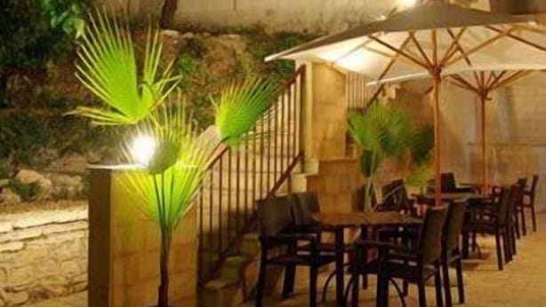 Un espace de restauration en plein air, avec des tables et des chaises, entouré de murs en pierre et agrémenté de plantes en pot.