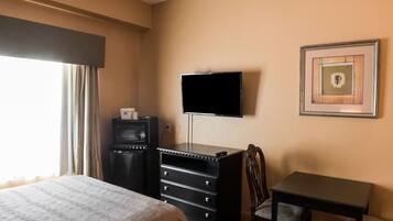 Habitación de hotel con cama, cómoda, televisor montado en la pared y un cuadro enmarcado.
