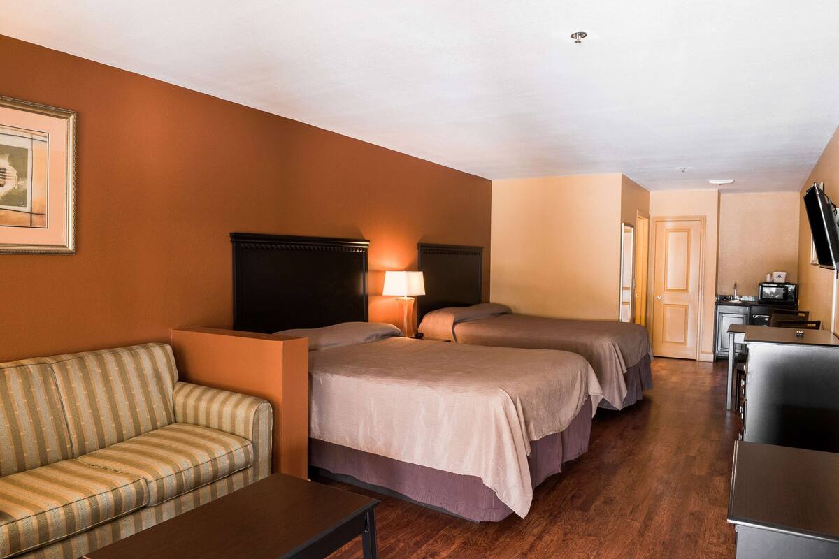 A hotel room with a sofa, two single beds, a desk, a television, and a lamp.