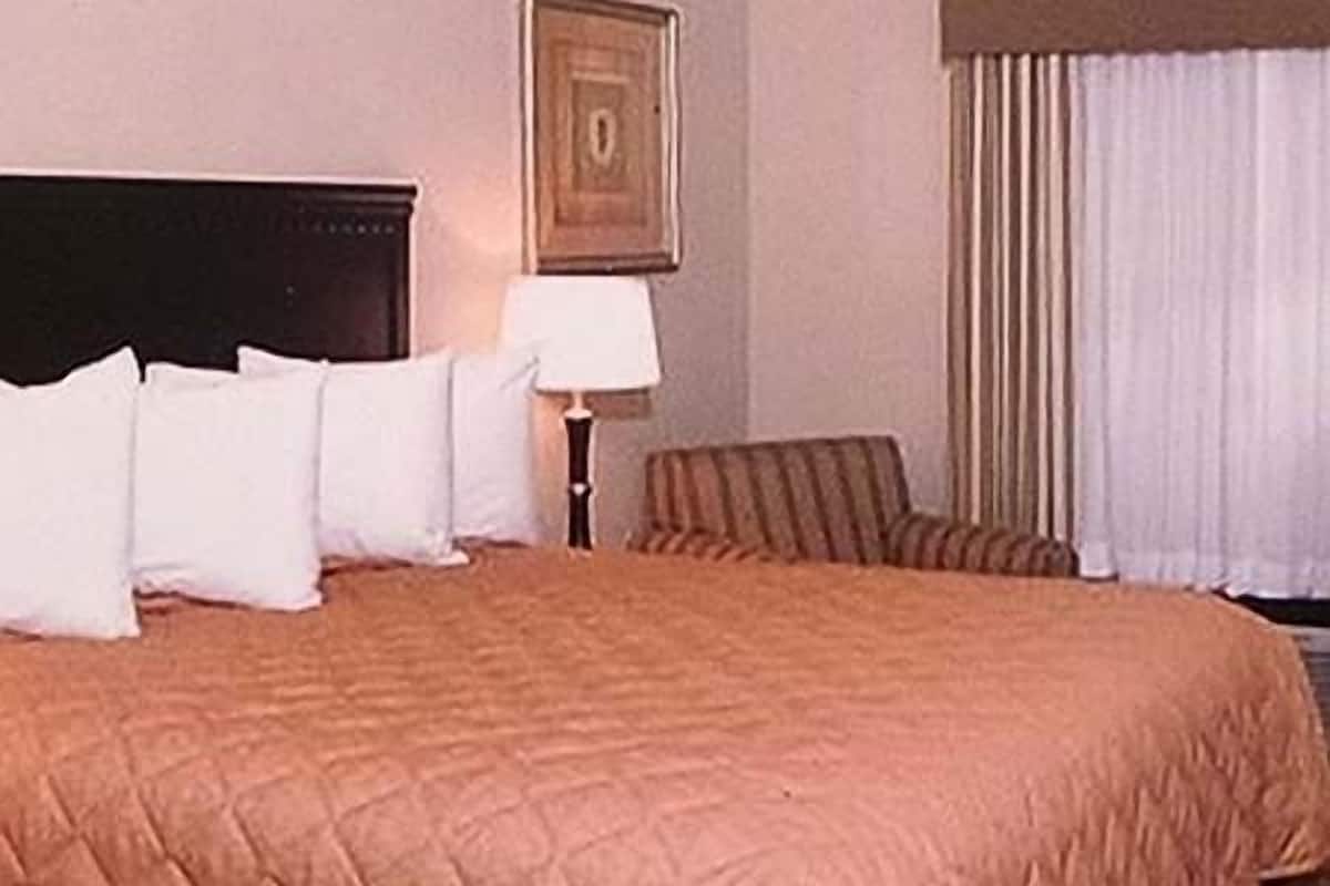 A neatly made bed with a brown quilt, a bedside lamp, and a framed picture on the wall.