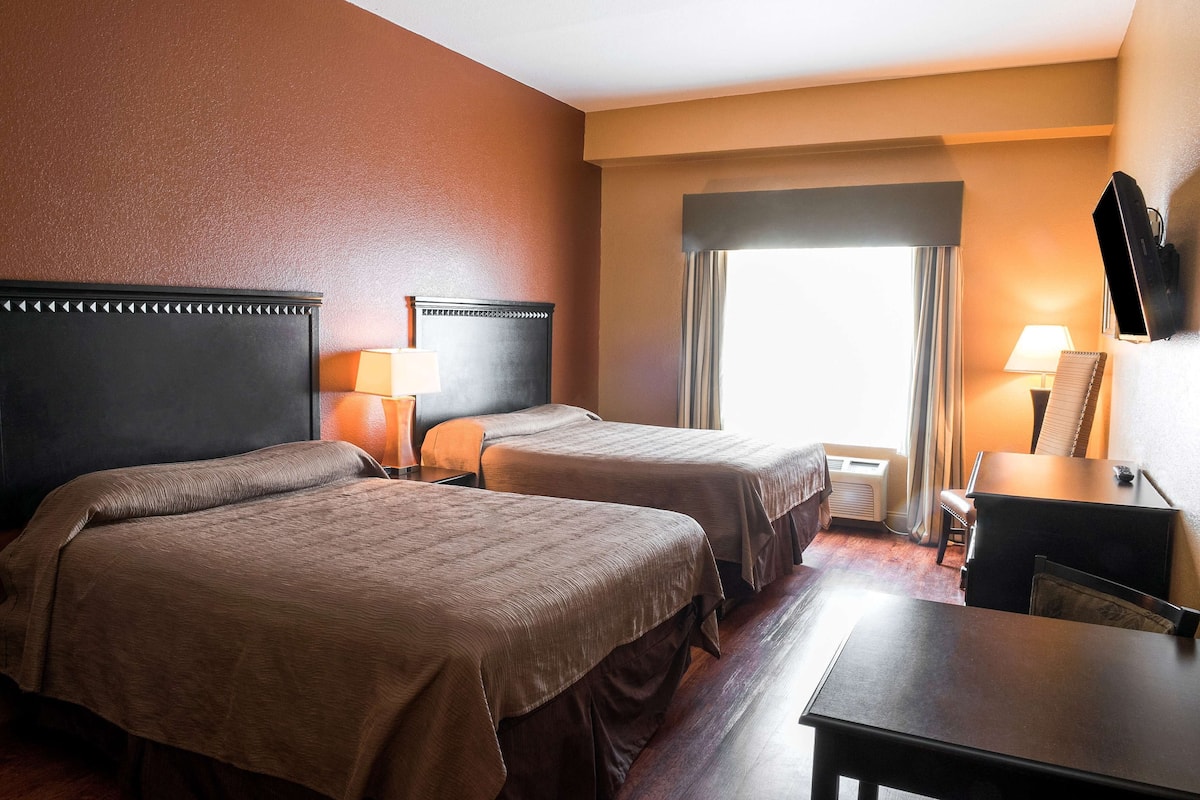 A hotel room with two beds, a desk, a chair, a TV, and a window with curtains.
