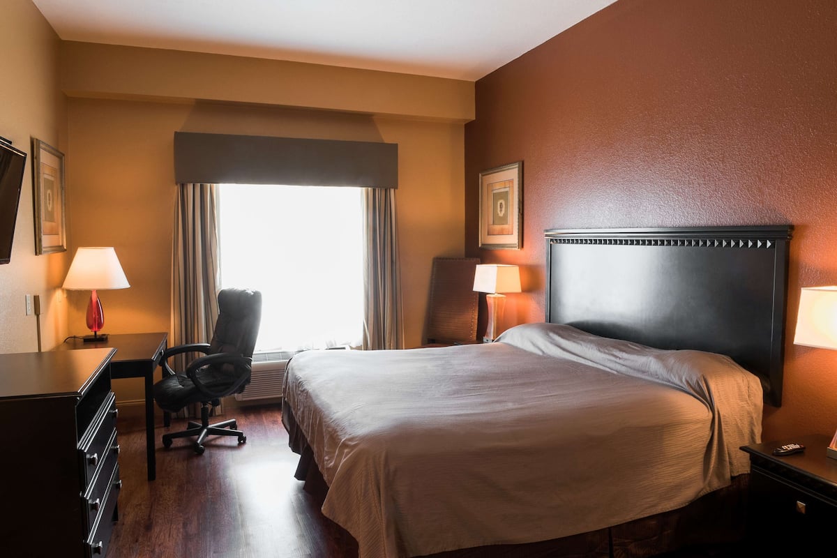 A hotel room with a large bed, a desk, a chair, and a window with curtains.
