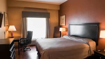 A hotel room with a large bed, a desk, a chair, and a window with curtains.