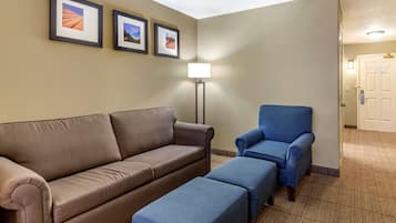 Habitación de hotel con un sofá marrón, un sillón azul y un reposapiés a juego. Se observan tres cuadros en la pared y una lámpara de pie.