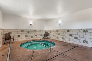A small indoor pool with a metal ladder, tiled walls, and a chair.