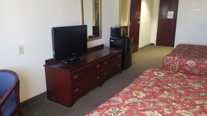 A hotel room with a bed, a TV on a dresser, a refrigerator, a mirror, and a door. - HomeTown Hotel Bryant (Bryant)