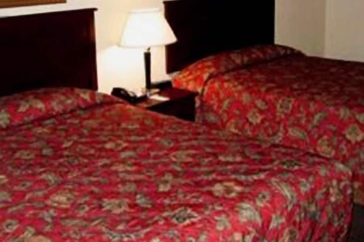 A hotel room with two beds, a nightstand with a lamp, and two framed pictures on the wall.
