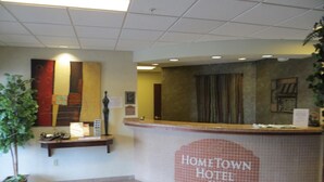 A reception area with a tiled wall displaying "Hometown Hotel" and a reception desk with a plant and informational materials. - HomeTown Hotel Bryant (Bryant)