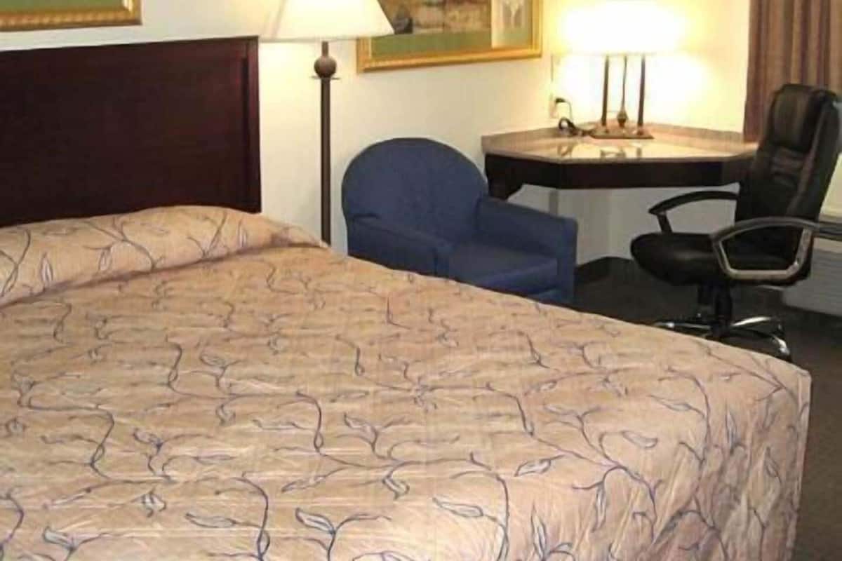 A hotel room with a bed, a desk, two chairs, and two lamps.