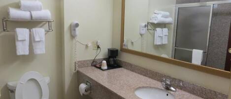 Un baño con inodoro, lavabo y espejo. Hay toallas en un estante y un secador de pelo en la pared.