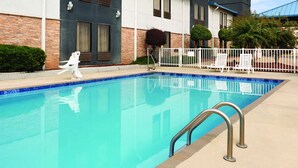 A swimming pool with a blue tiled edge, white lounge chairs, and a metal pool ladder. - HomeTown Hotel Bryant (Bryant)