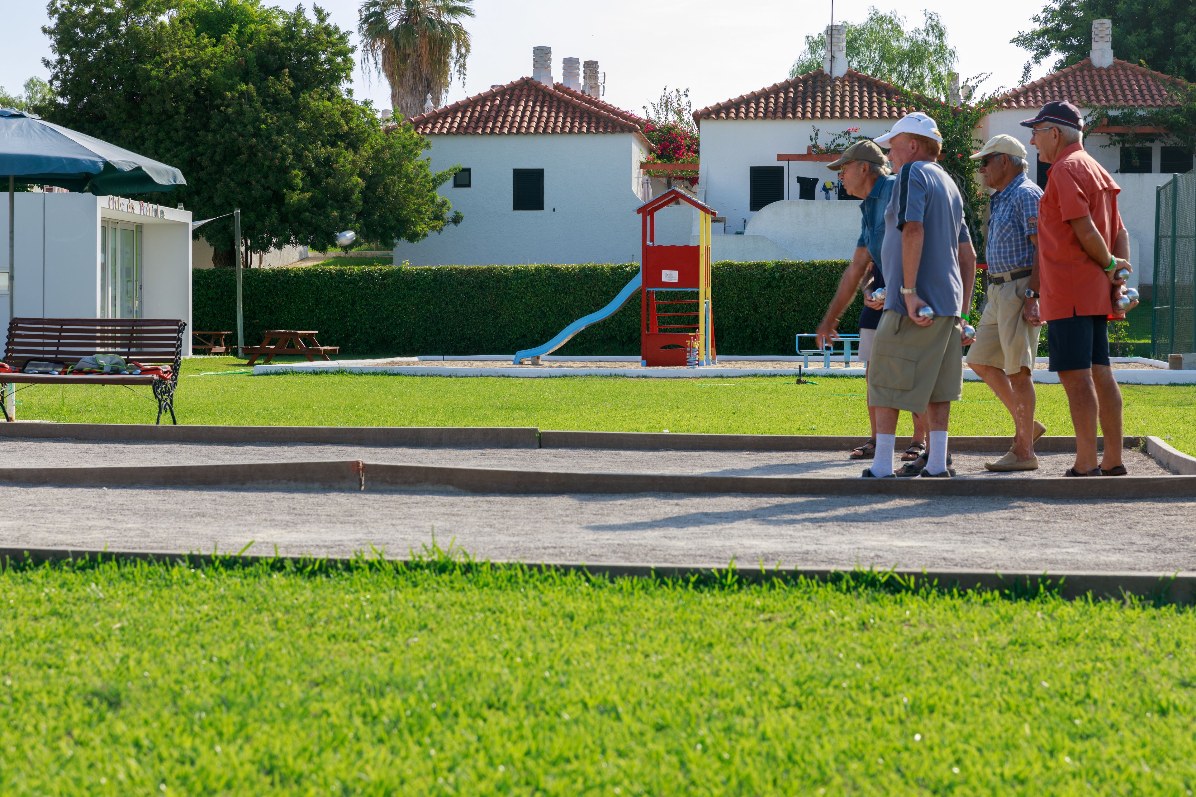 A park with a playground, benches, and a building with a red roof.