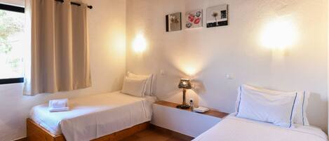 A room with two beds, a nightstand, and a lamp. There are wall-mounted lights and a window with curtains.