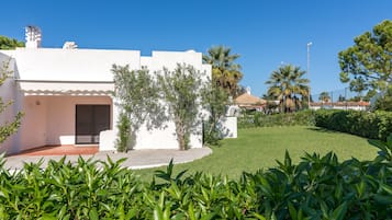 Un edificio blanco con un acceso cubierto, rodeado de abundante vegetación y palmeras.