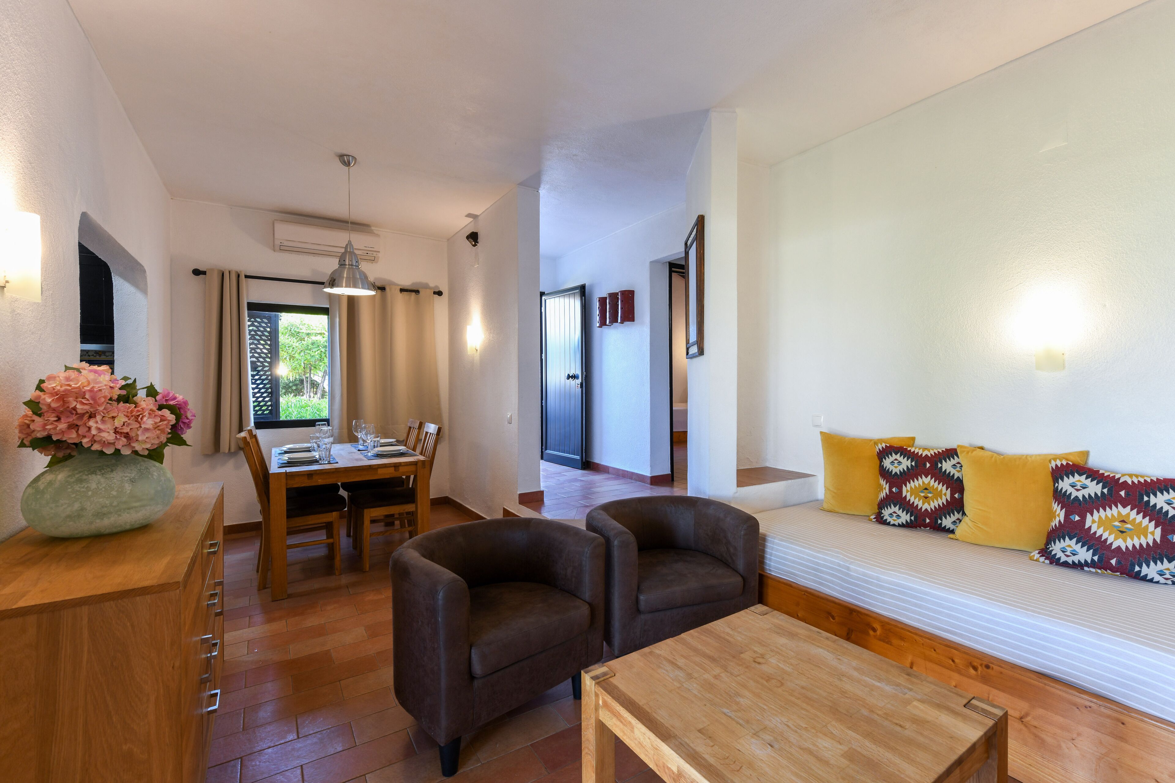 Una sala moderna con un sofá, dos sillones, una mesa de centro de madera y un comedor con mesa y sillas.