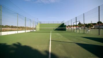 Una cancha de tenis con red, rodeada por una cerca de malla metálica, y un cielo despejado arriba.