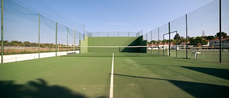 A tennis court with a net, surrounded by a chain-link fence, and a clear sky above.